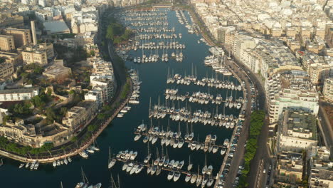 Sailboats-and-regular-Boats-sitting-in-Marina-Port-on-Malta-Island,-Aerial-tilt-down-View