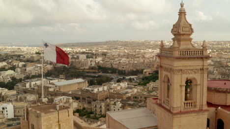 Beautiful-Gozo-Sand-Castle-Fort-with-Malta-Flag-waving-revealing-Countryside-of-Gozo-Island,-Aerial-forward-dolly