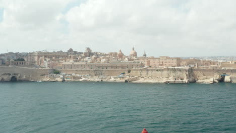 Malta-Hauptstadt-Valletta-Aus-Meerblick,-Luftwagen-Nach-Vorne-In-Richtung-Beige-Stadt-Im-Blauen-Wasser-Im-Vordergrund