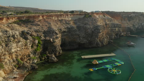 Tropical-Anchor-Bay-by-Popeye-Village-on-Malta-Gozo-Island,-Malta-with-Water-platform-to-play-with-no-people-at-Sunset-with-Green-Turquoise-Water,-Aerial-View