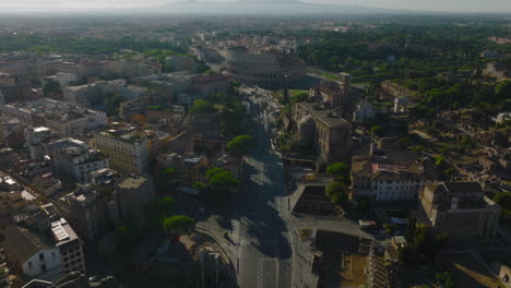High-angle-view-of-road-and-buildings-in-city-at-golden-hour.-Tilt-up-reveal-historic-ancient-Colosseum-amphitheatre.-Rome,-Italy