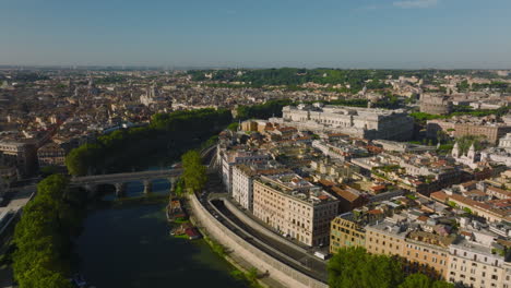 Aerial-cinematic-footage-of-Tiber-river-bend-and-buildings-on-waterfront.-River-lined-by-rows-of-green-trees.-Rome,-Italy