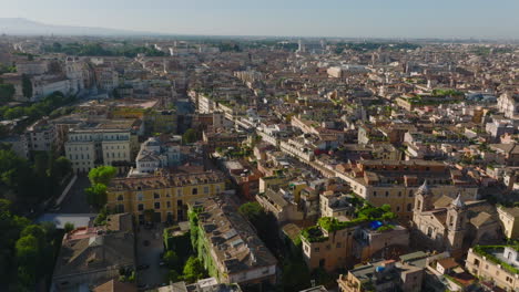 Aerial-descending-footage-of-old-town-development-in-historic-city-centre.-Buildings-and-landmarks-lit-by-bright-morning-sun.-Rome,-Italy
