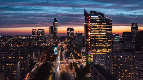Fly-forwards-above-wide-downtown-boulevard.-Amazing-hyperlapse-of-straight-multilane-main-road-leading-between-modern-skyscrapers-against-sunset-sky.-Warsaw,-Poland