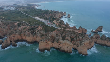 Spectacular-aerial-drone-view-of-Lagos,-Portugal-coast-ocean-with-lighthouse-and-townscape-on-background,-day,-circle-pan