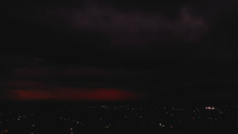 Sliding-aerial-footage-of-red-clouds-in-sky-with-flashing-lightning-during-thunderstorm.-Streetlights-in-town.-Valladolid,-Mexico