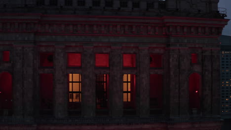 Tight-slider-of-red-illuminated-historic-building.-Downtown-skyscrapers-at-dusk-in-background.-Warsaw,-Poland