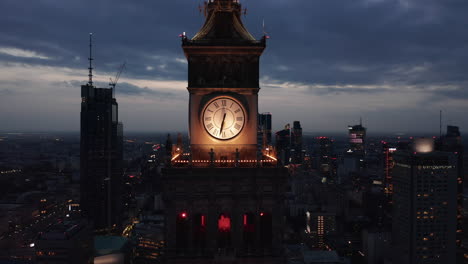 Pull-back-footage-of-tower-clock-on-top-of-high-rise-building.-Evening-aerial-view-of-downtown-skyscrapers.-Warsaw,-Poland