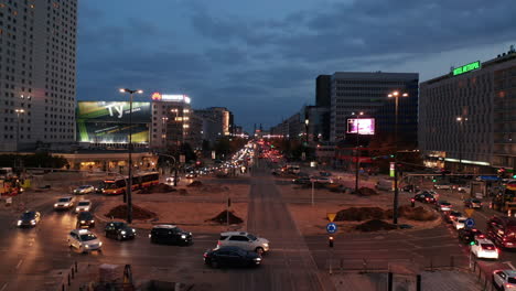 Evening-traffic-in-city-centre.-Cars-driving-through-large-roundabout-crossed-by-tram-tracks.-Busy-streets-at-twilight.-Warsaw,-Poland