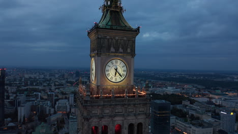 Fly-around-Tower-clock.-Large-illuminated-clock-face-and-lookout-terrace-above-city-in-twilight-time.-Warsaw,-Poland