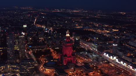 Slide-and-pan-shot-red-lit-Palace-of-Culture-and-Science-at-night.-Aerial-panoramic-footage-of-Russian-style-high-rise-building.-Warsaw,-Poland