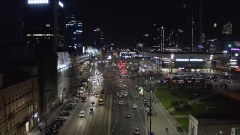 Rising-footage-of-heavy-traffic-in-city-centre-at-night.-Wide-multilane-road-leading-between-high-rise-buildings-and-train-station.-Warsaw,-Poland