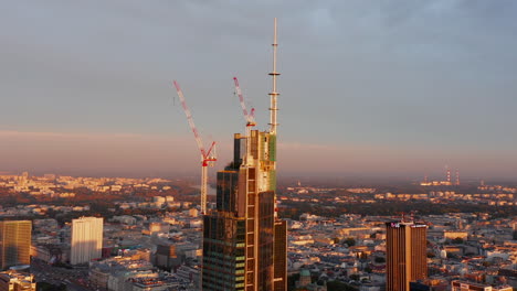 Orbit-around-shot-of-top-of-skyscraper-construction-site-with-cranes-lit-by-bright-morning-sun.-Warsaw,-Poland