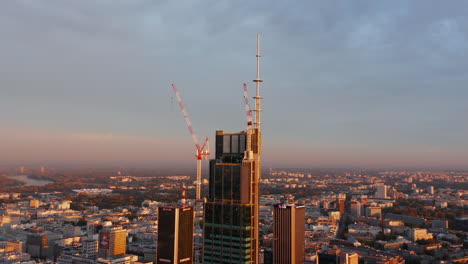 Construction-of-new-modern-high-rise-downtown-building.-Tower-cranes-on-site.-Scene-lit-by-morning-sun.-Warsaw,-Poland