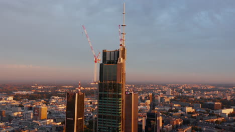 Morning-forwards-fly-towards-construction-site-of-tall-downtown-office-of-apartment-building.-Warsaw,-Poland