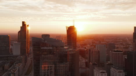 Aerial-footage-of-downtown-skyscrapers-against-bright-light-at-sunset.-Traffic-in-wide-streets.-Warsaw,-Poland