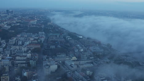 Fly-above-morning-city.-Buildings-in-urban-neighbourhood-and-Vistula-river-shrouded-in-mist.-Warsaw,-Poland