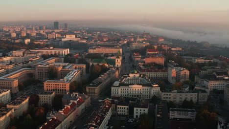 Morning-aerial-view-of-buildings-in-town-at-sunrise-time.-Fog-around-river-in-background.-Warsaw,-Poland