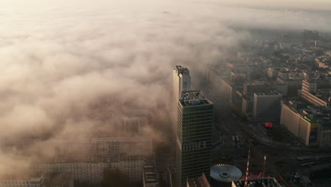 Fly-above-large-city.-Busy-road-between-high-rise-buildings.-Morning-fog-cover-illuminated-by-rising-sun.-Warsaw,-Poland