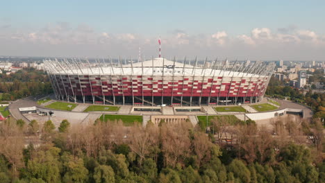 Ascending-shot-of-modern-multifunction-arena,-PGE-narodowy,--national-stadium.-Revealing-buildings-in-city-in-background.-Warsaw,-Poland