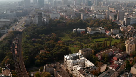 Backwards-fly-above-park-in-urban-neighbourhood.-Tilt-up-reveal-of-skyline-with-downtown-skyscrapers-against-bright-sky.-Warsaw,-Poland