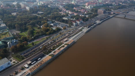 High-angle-view-of-heavy-traffic-on-trunk-road-leading-along-Vistula-river.-Tilt-up-reveal-cityscape-with-Royal-Castle.-Warsaw,-Poland