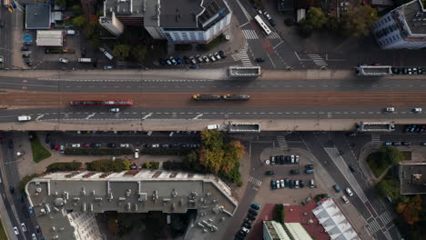 Aerial-birds-eye-overhead-top-down-panning-view-of-transport-in-city.-Pair-of-trams-passing-by-each-other-on-elevated-road-with-tram-tracks.-Warsaw,-Poland