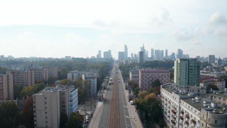 Backwards-fly-above-wide-and-straight-boulevard-in-city.-Multilane-road-and-tram-track.-Skyline-with-modern-high-rise-office-buildings.-Warsaw,-Poland