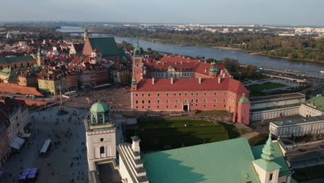 Aerial-panoramic-footage-of-Royal-castle-complex,-Castle-square-and-churches-in-old-town-in-golden-hour.-Vistula-river-flowing-in-background.-Warsaw,-Poland