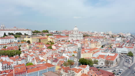 Aerial-wide-dolly-in-view-of-colorful-traditional-old-houses-and-church-on-the-hills-urban-city-center-of-Lisbon,-Portugal