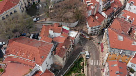 Aerial-overhead-view-of-a-yellow-tram-turning-a-corner-on-the-tracks-in-urban-city-center-of-Lisbon,-Portugal