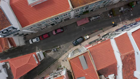Aerial-birds-eye-overhead-top-down-view-of-narrow-street-in-old-town-center.-Parking-cars-on-side-of-road-and-person-walking-on-sidewalk.-Zooming-in-from-drone.-Lisbon,-capital-of-Portugal.