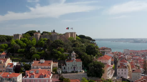 Elevated-view-of-medieval-Saint-George-Castle-above-historic-houses-in-downtown.-Stone-walls-and-fortification.-Drone-camera-flying-around.-Lisbon,-capital-of-Portugal.