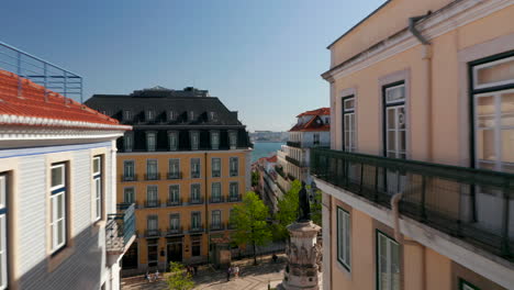 Drone-camera-flying-in-top-floor-level-above-narrow-streets-towards-rivershore.-Lisbon,-capital-of-Portugal.
