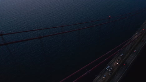 Aerial-view-of-cars-driving-on-25th-of-April-Bridge-after-sunset.-Drone-flying-forwards-and-rotating.-Lisbon,-capital-of-Portugal.