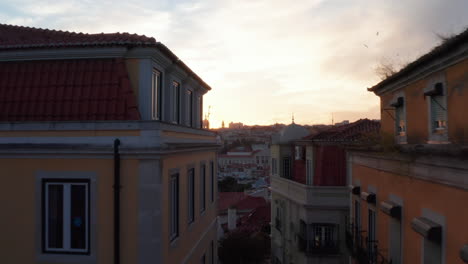 Aerial-dolly-in-reveal-of-house-rooftops-and-churches-in-urban-city-center-of-Lisbon,-Portugal-during-sunset