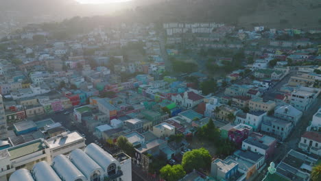 Forwards-fly-above-low-colourful-houses-in-residential-Bo-Kaap-borough.-Aerial-view-of-traditional-development-against-sun.-Cape-Town,-South-Africa