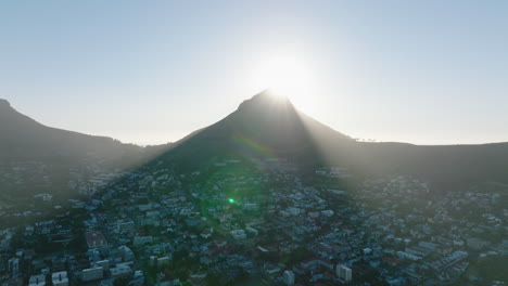 Aerial-descending-shot-of-Lions-Head-mountain-casting-shadow-residential-borough.-View-against-sun.-Cape-Town,-South-Africa