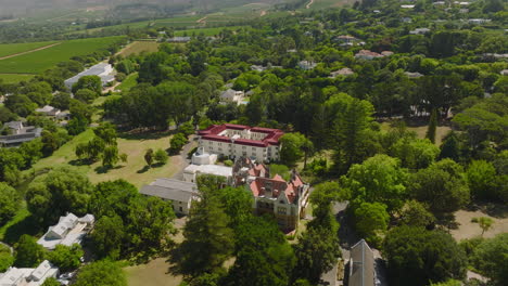 Aerial-footage-of-palace-or-luxury-residence-in-park.-Slide-and-pan-shot-of-buildings-between-green-trees.-Cape-Town,-South-Africa