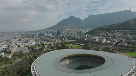 Aerial-view-into-modern-football-arena.-Cityscape-with-harbour-and-high-mountains-in-distance.-Cape-Town,-South-Africa