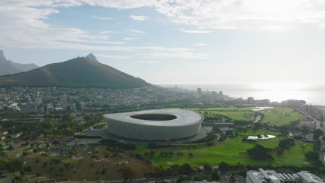 Dia-Und-Schwenk-Einer-Futuristischen-Struktur.-Modernes-Fußballstadion,-Umgeben-Von-Einem-Golfplatz.-Gebäude-Im-Ferienort-An-Der-Ozeanküste.-Kapstadt,-Süd-Afrika