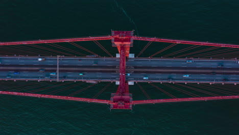 Overhead-aerial-view-of-busy-car-traffic-across-Ponte-25-de-Abril-red-bridge-in-Lisbon,-Portugal