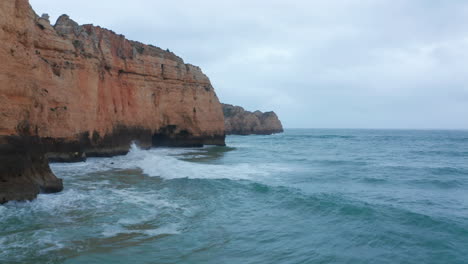 Szenischer-Hintergrund-Banner-Luftdrohne-Blick-Auf-Die-Küste-Von-Lagos-Mit-Wellen,-Die-An-Bewölkten-Tag-Gegen-Klippen-Krachen,-Portugal
