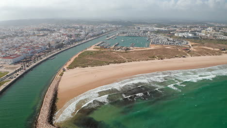Szenische-Lagos-strandküste-In-Algarve,-Portugal.-Luftdrohnenansicht,-Die-Rückwärts-über-Dem-Ozean-Fliegt,-Mit-Portugiesischem-Stadtbild-Im-Hintergrund,-Sonniger-Tag