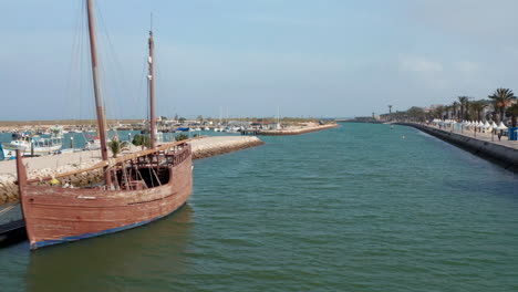 Lagos-Hafenkanal-Mit-Portugiesischem-Holzboot-Caravela-Verankert-Auf-Dock.-Luftdrohne,-Die-Oben-Nach-Vorne-über-Wasser-Fliegt,-Portugal,-Tag
