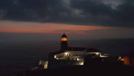 Scenic-aerial-view-of-beautiful-romantic--Ponta-da-Piedade-Lighthouse-in-Lagos-Algarve,-Portugal,-drone-flying-foward-towards-yellow-fresnel-lens-head,-evening-dusk