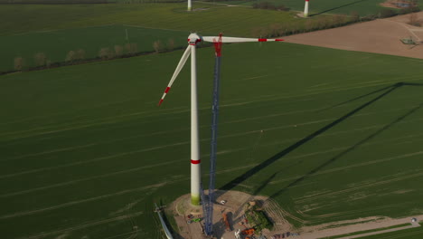 High-angle-view-of-tall-crane-near-wind-turbine-under-construction.-Completing-large-propeller.-Green-energy,-ecology-and-carbon-footprint-reduction-concept