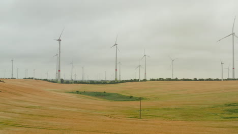 Forwards-fly-above-grain-field-surrounded-by-wind-power-stations.-Large-spinning-rotors-on-tall-towers.-Green-energy,-ecology-and-carbon-footprint-reduction-concept