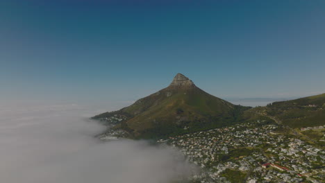 Aerial-panoramic-shot-of-Lions-Head-mountain-towering-above-residential-neighbourhood-and-sea-coast-covered-with-dense-fog.-Cape-Town,-South-Africa