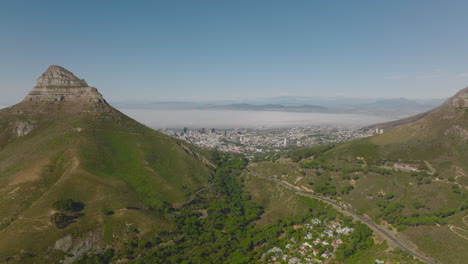Aerial-panoramic-footage-of-large-city-behind-mountains-pass.-Sunny-day-with-fog-in-background.-Cape-Town,-South-Africa